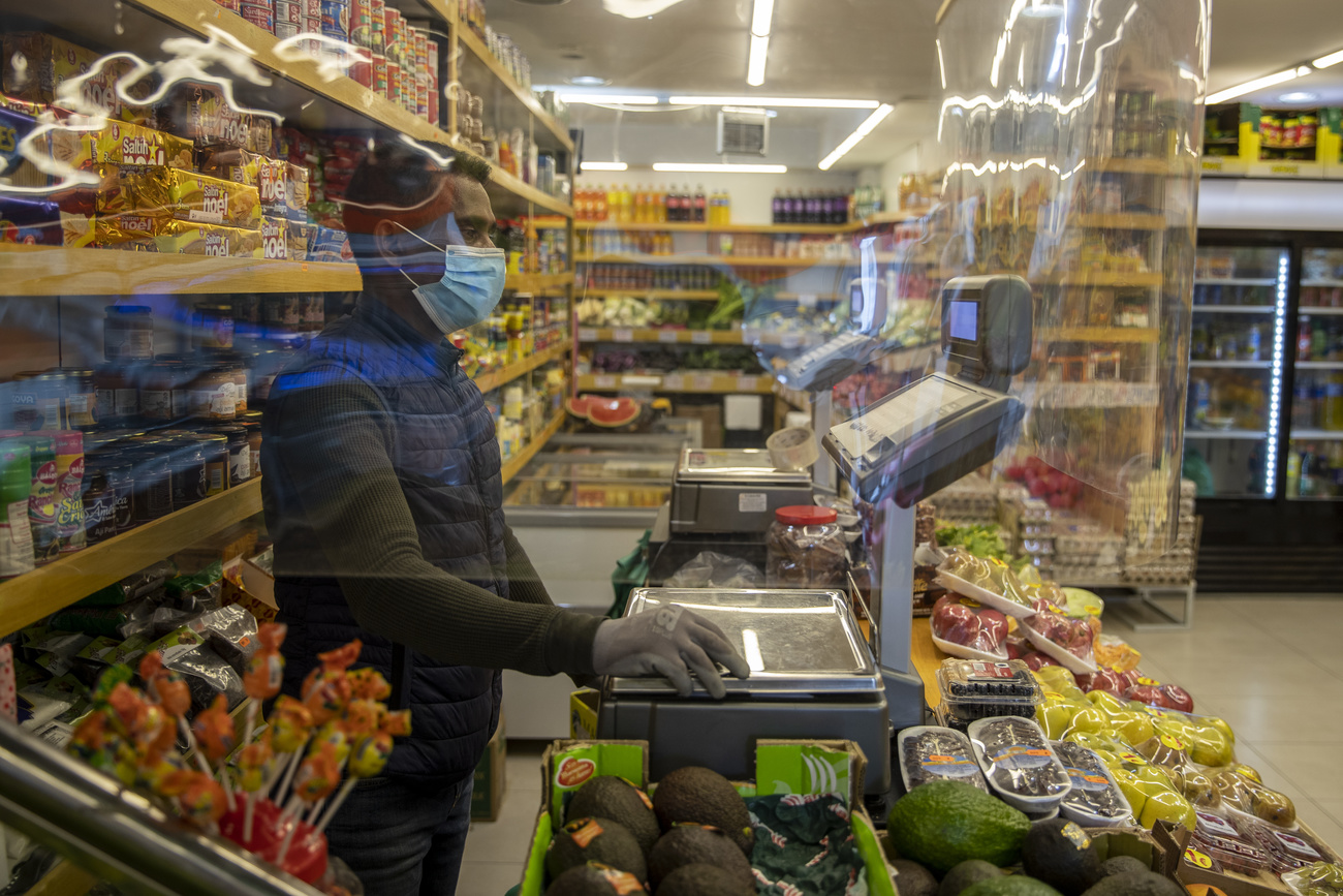 Interno di un negozio di alimentari con addetto completamente bardato e schermato da plexiglass