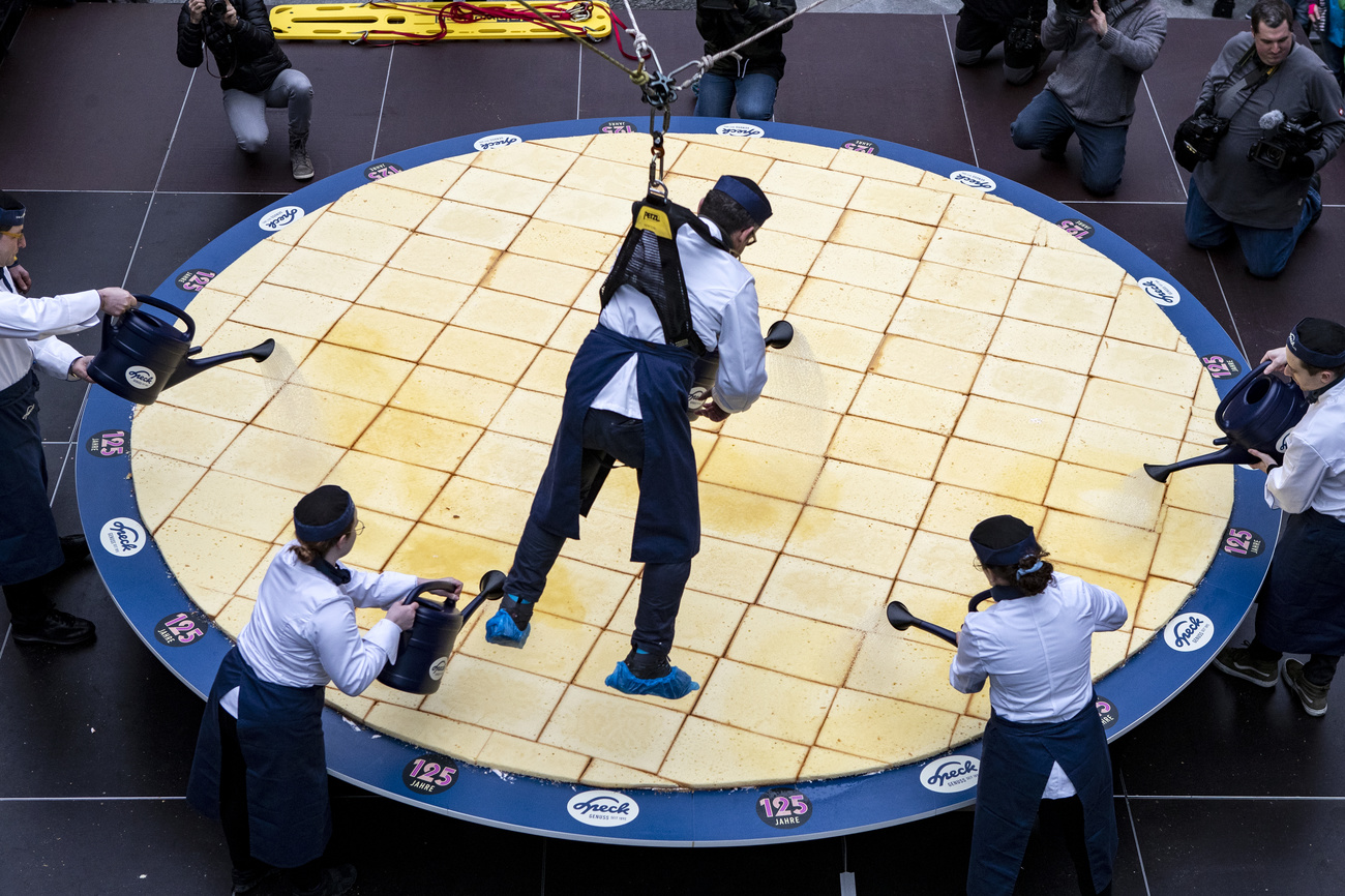 A man hangs over a large cake on a winch