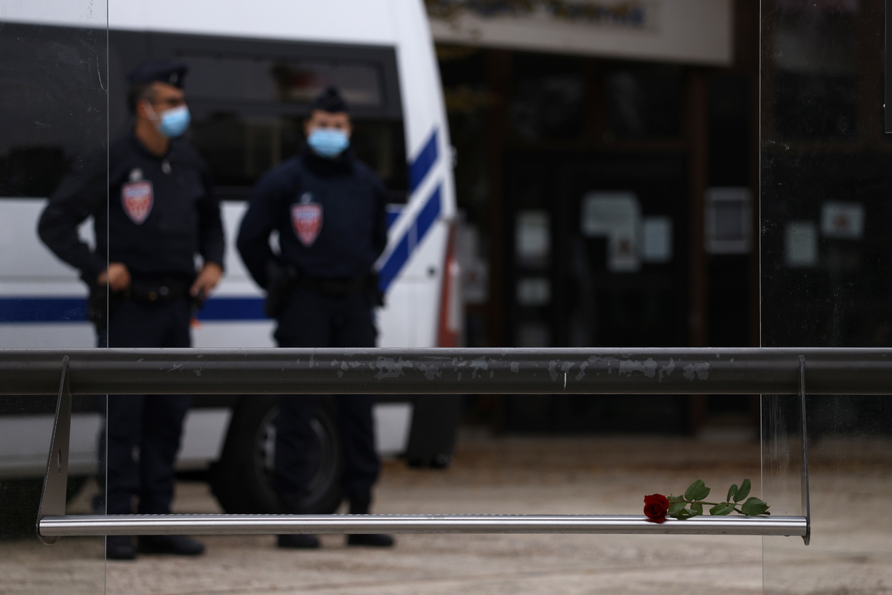 Due gendarmi francesi all erta nei pressi di un furgone. Si intravede, sfuocata, l entrata di una scuola.