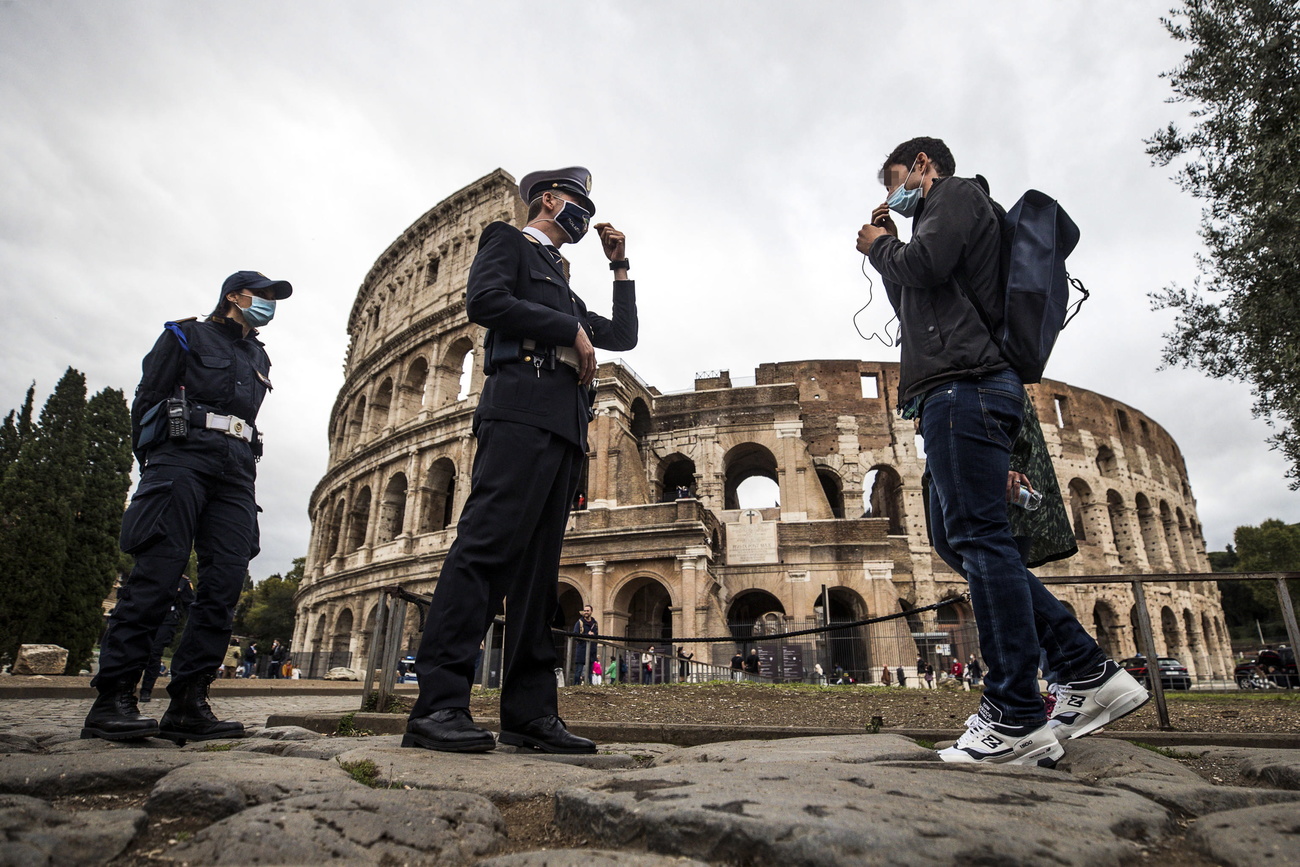 Due poliziotti invitano un giovane turista a indossare la mascherina davanti al Colosseo.
