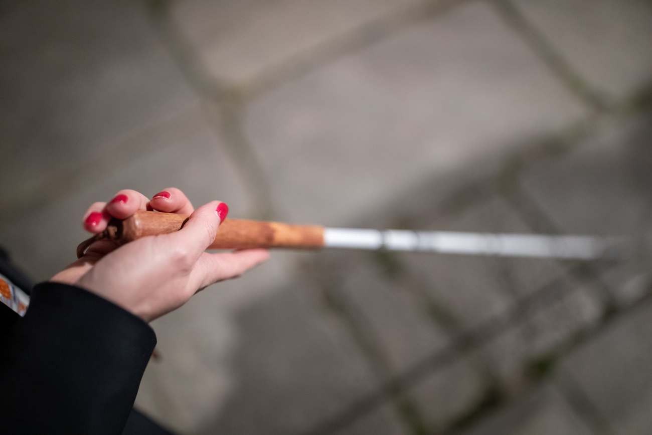 Primissimo piano di mano di donna con smalto rosso alle unghie impugna un bastone bianco; contesto sfuocato