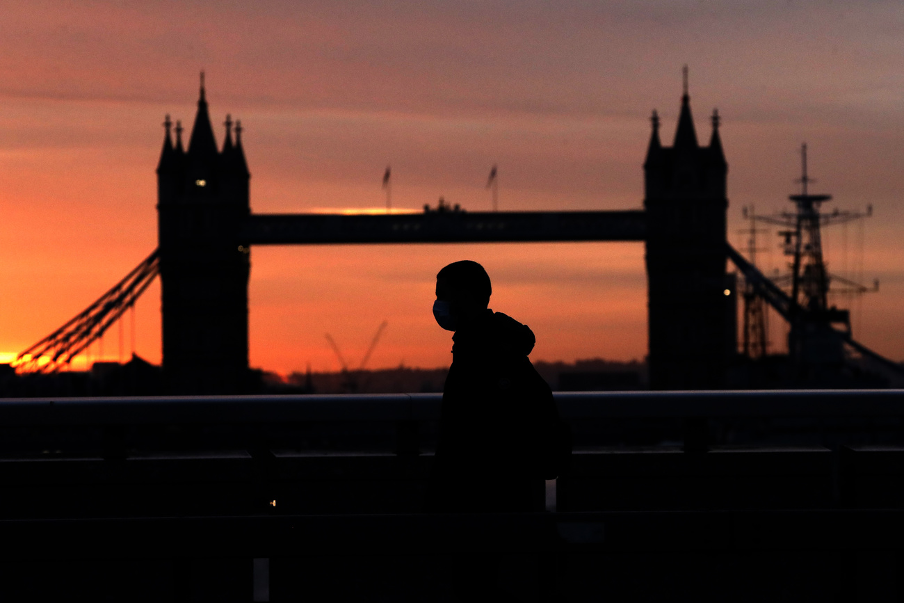 Una persona con mascherina passeggia al crepuscolo nei pressi del ponte di Londra.