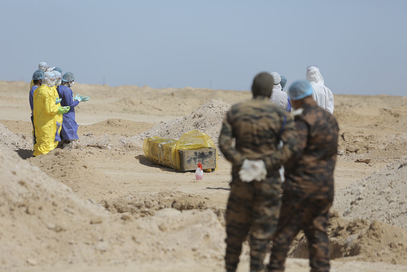 Persone con tute protettive pregano davanti a una bara di legno