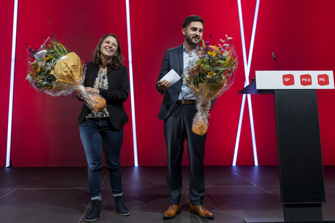 Una donna e un uomo con un mazzo di fiori ciascuno sorridono accanto a un pulpito con scritto SP-PS