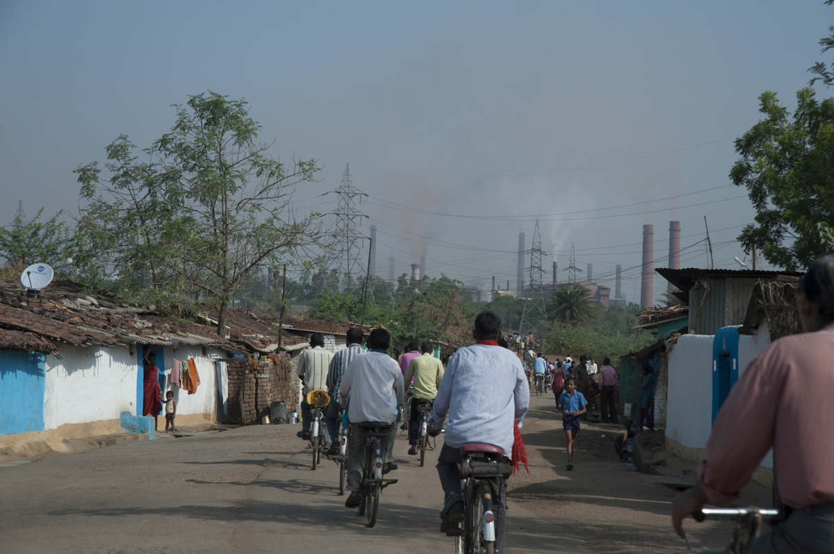 Men on bycicles riding the Steel Plant in the distance.