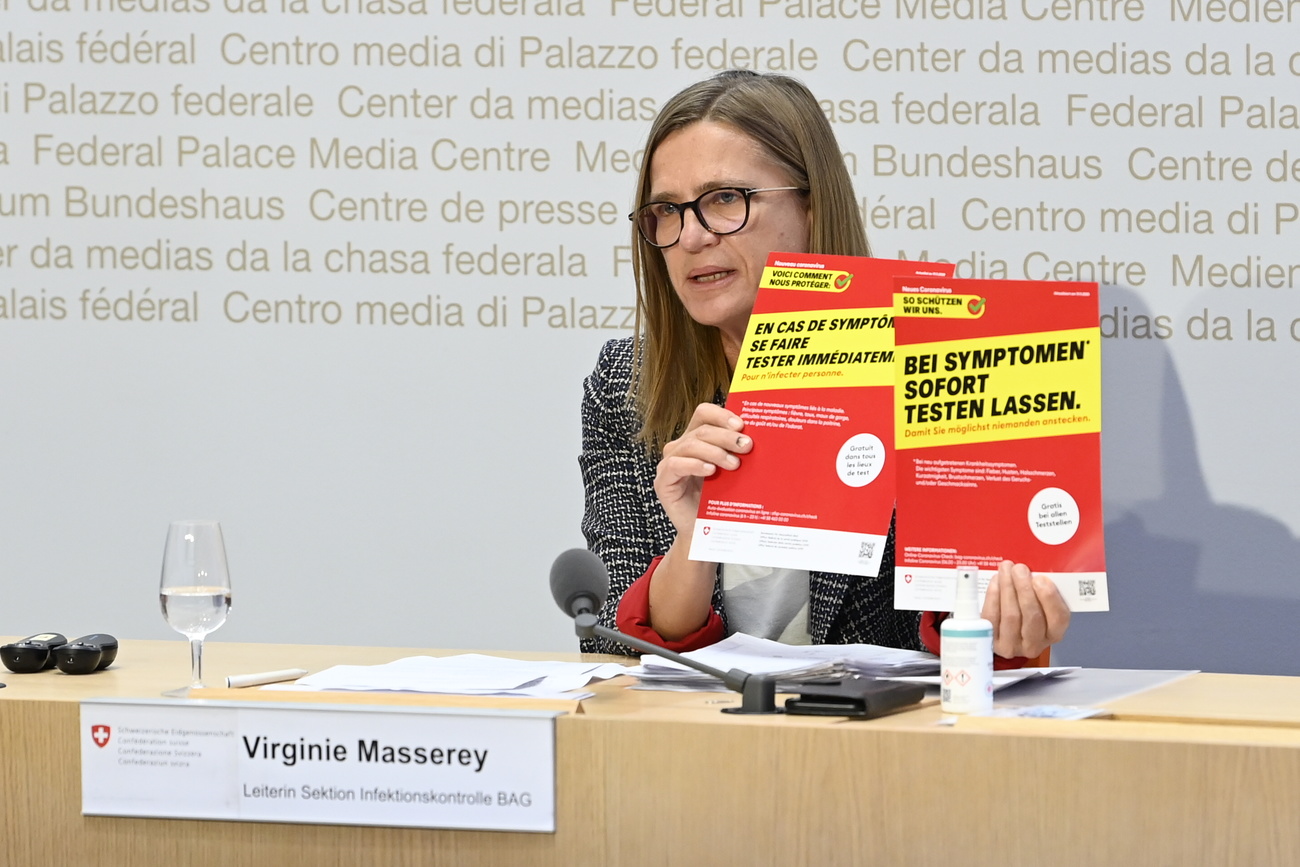 Virginie Masserey al tavolo di conferenza stampa mostra due manifesti che raccomandano i test