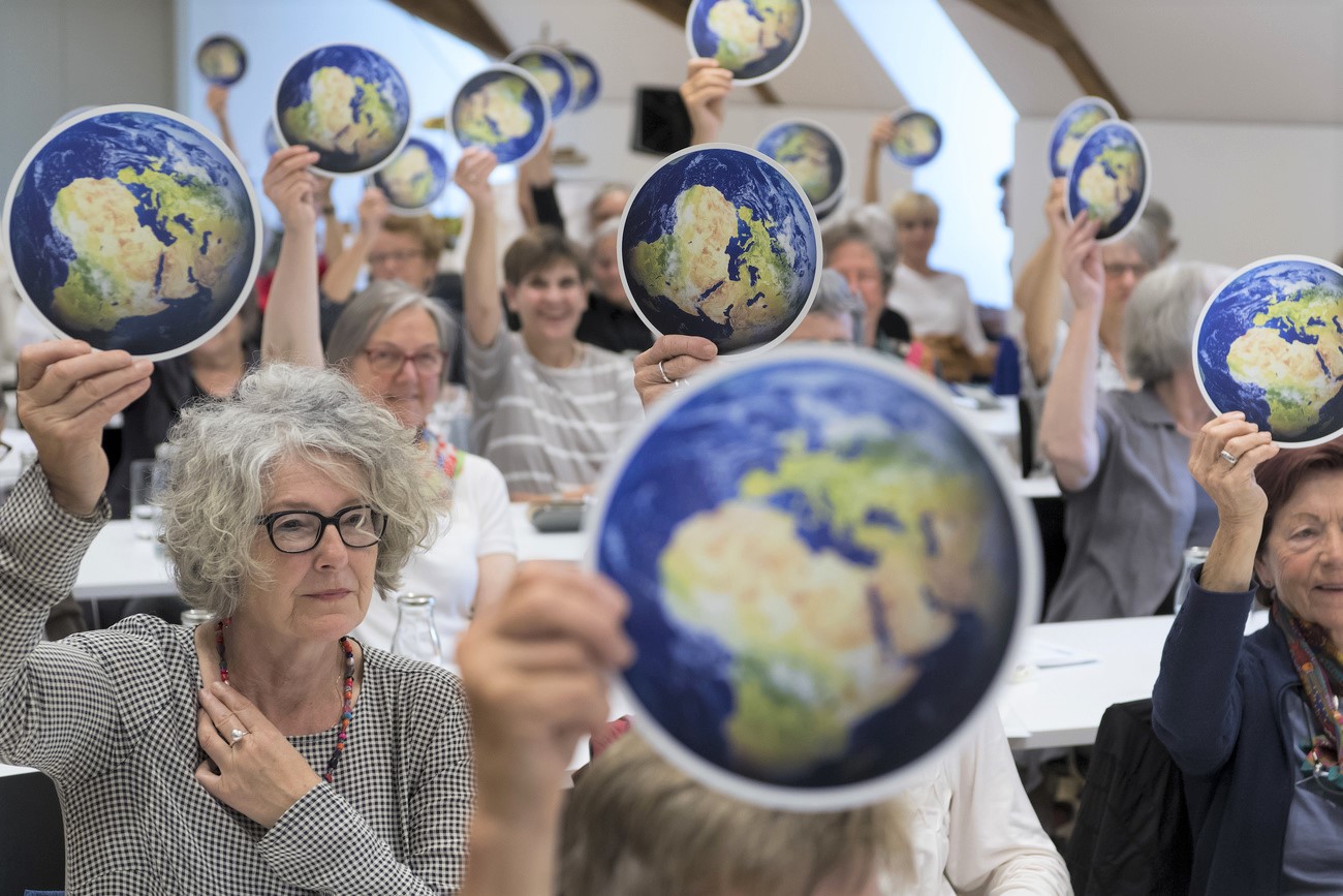 Women hold up a round card depicting the Earth