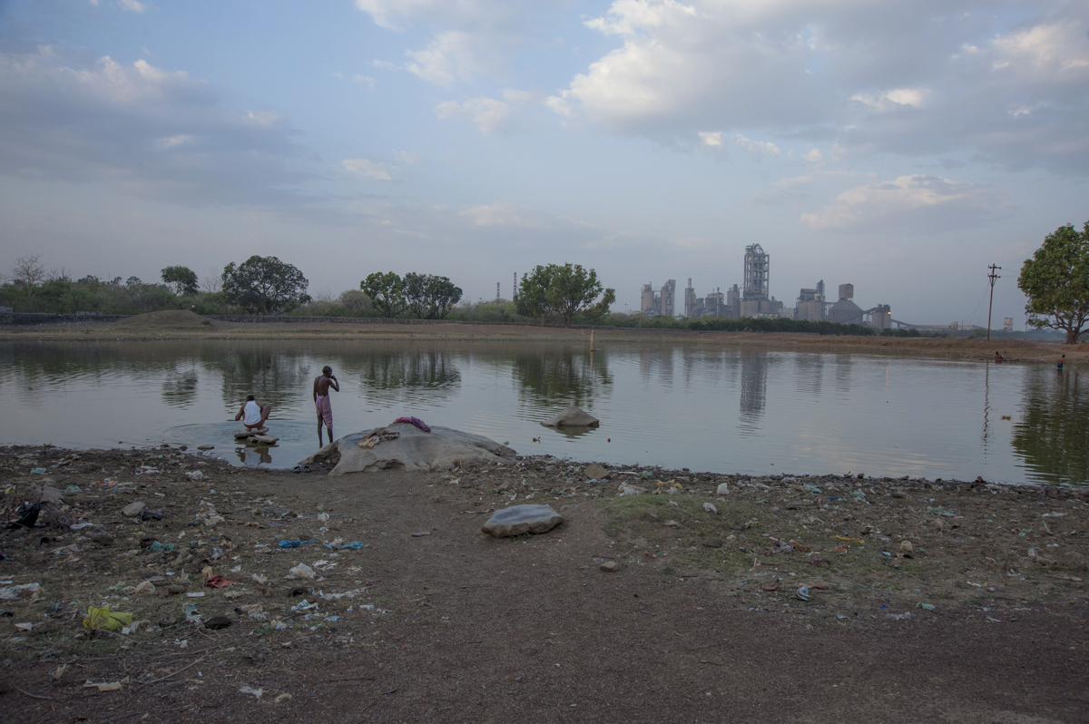 A littered pond, in the distance Ambuja-Holcim.