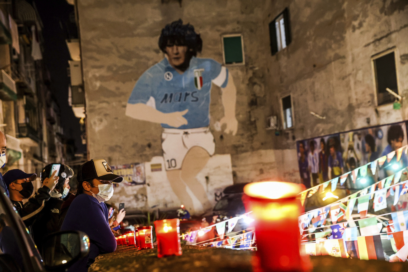 Vicolo di città vecchia con murale che raffigura Maradona con maglia del Napoli e lumini allineati in basso.