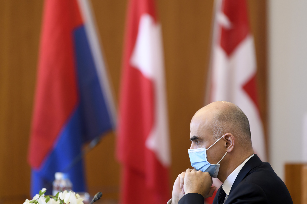Alain Berset fotografato di lato con mascherina e sullo sfondo le bandiere della Svizzera e del Ticino.