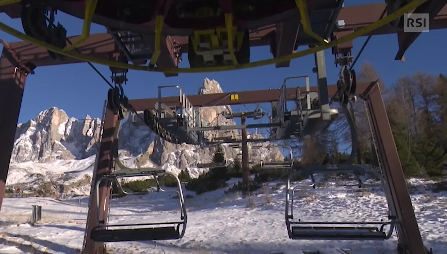 Primo piano di seggiovia ferma e con posti completamente vuoti; sul fondo, dolomiti