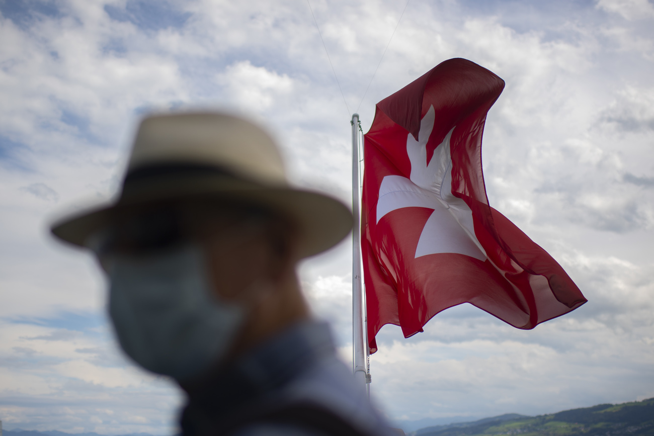 Blurred picture of man with hat and mask in front of Swiss flag