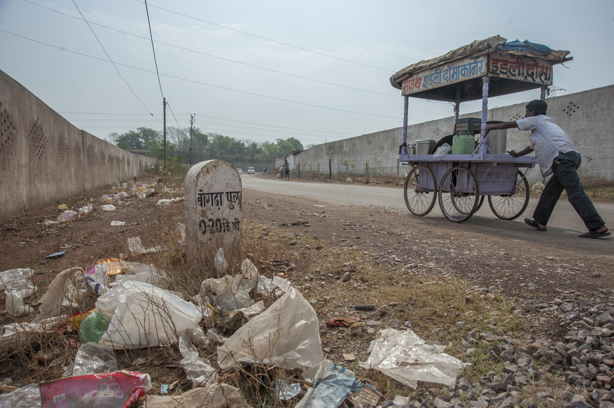 On a littered street in India a man pushes a cart.