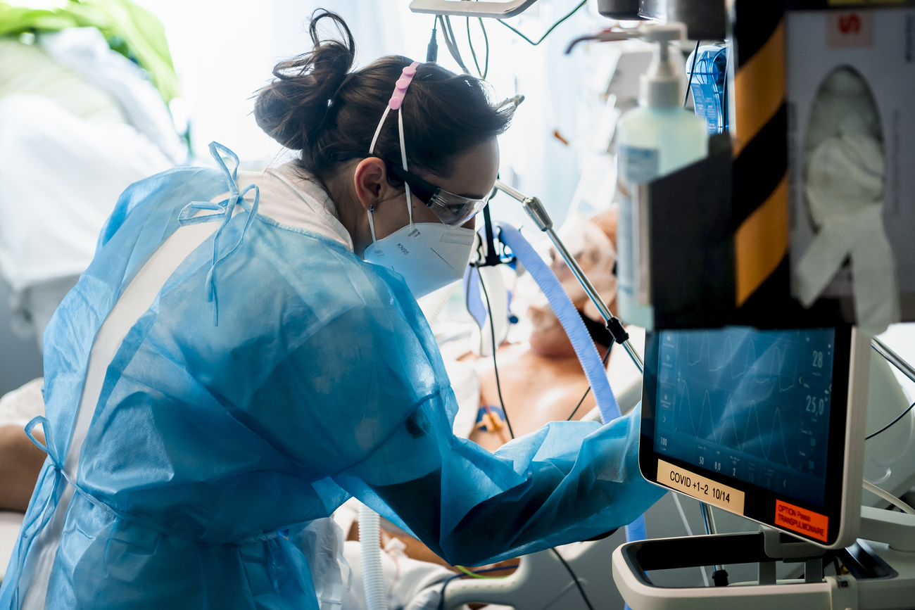 Infermiera completamente coperta da dispositivi di protezione cura un paziente in terapia intensiva