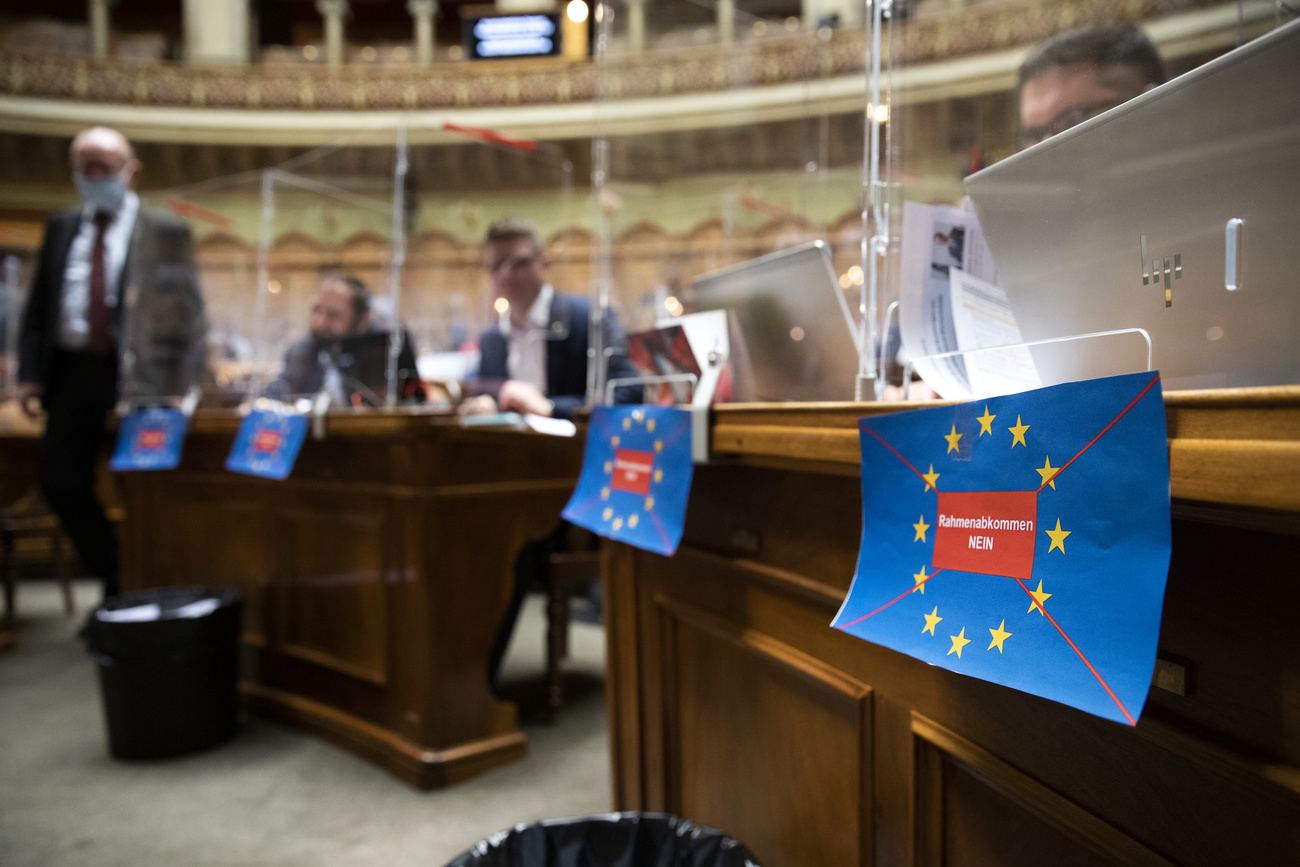 un uomo in piedi in parlamento e sullo sfondo dei cartelli con la scritta: Accordo quadro - No.