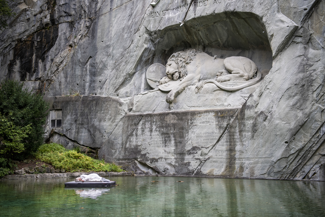 Artista recostada en una balsa frente a estatua de león muerto y en la misma posición