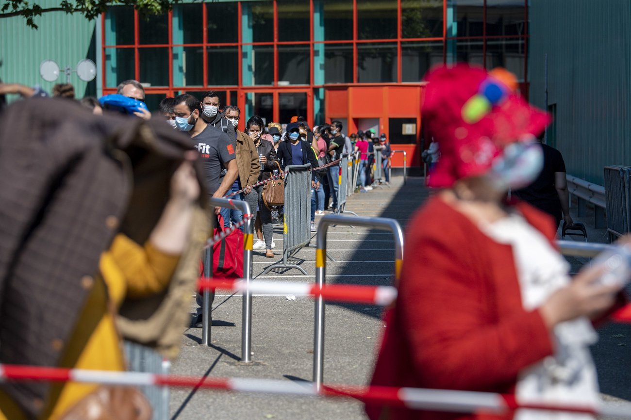 Persone in coda lungo transenne fuori da quello che appare come un palazzetto dello sport