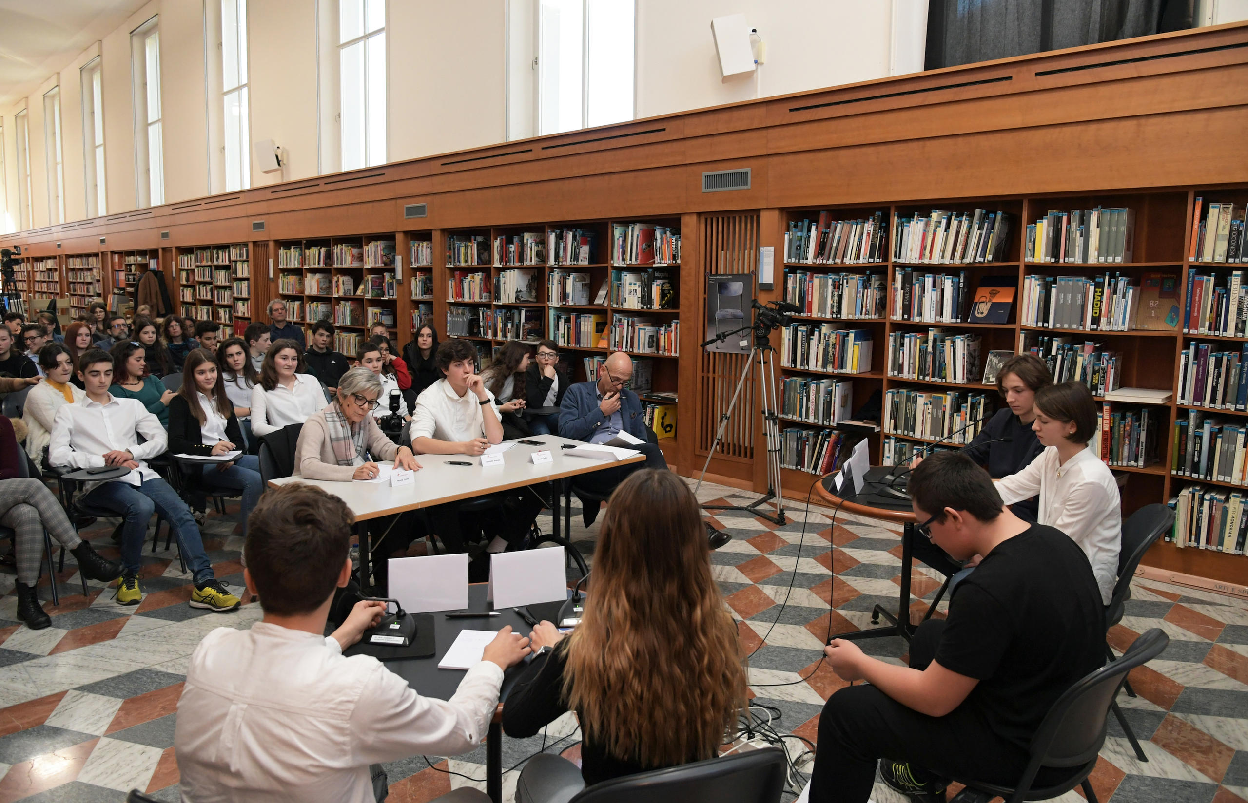 quattro ragazzi che dibattono davanti ai loro compagni in una biblioteca.