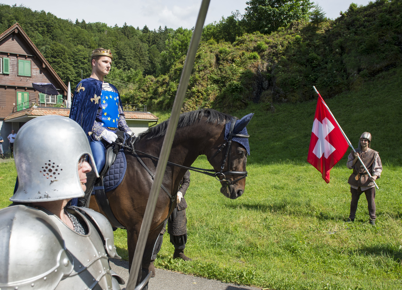 uomo a cavallo travestito da re, con la bandiera dell UE e uno in piedi che sventola quella della Svizzera