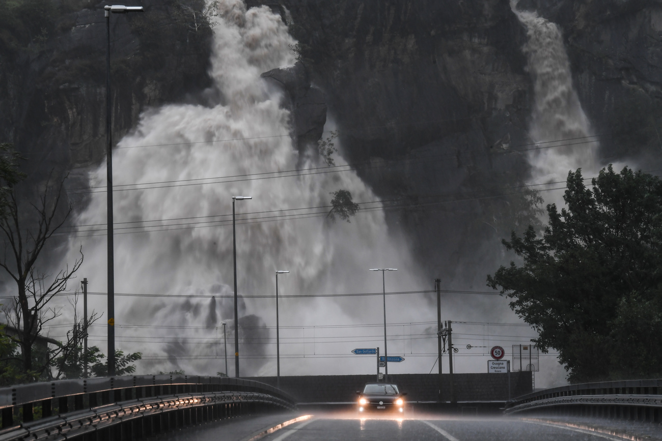 Un auto circula en medio de la tormenta, detrás se observa un torrente de agua que baja por la montaña