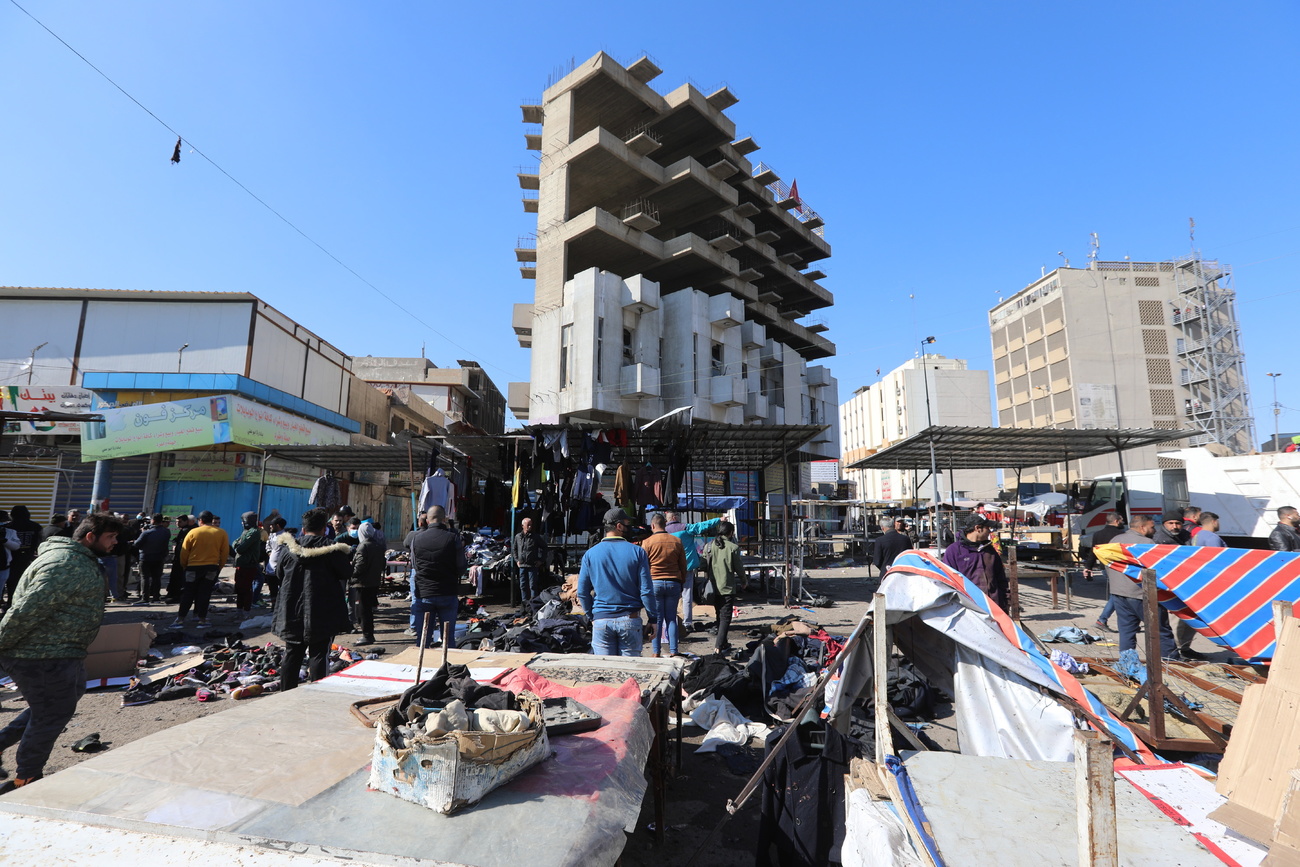 Una piazza di città mediorientale con bancarelle di vestiti divelte e macchie di sangue e sparse