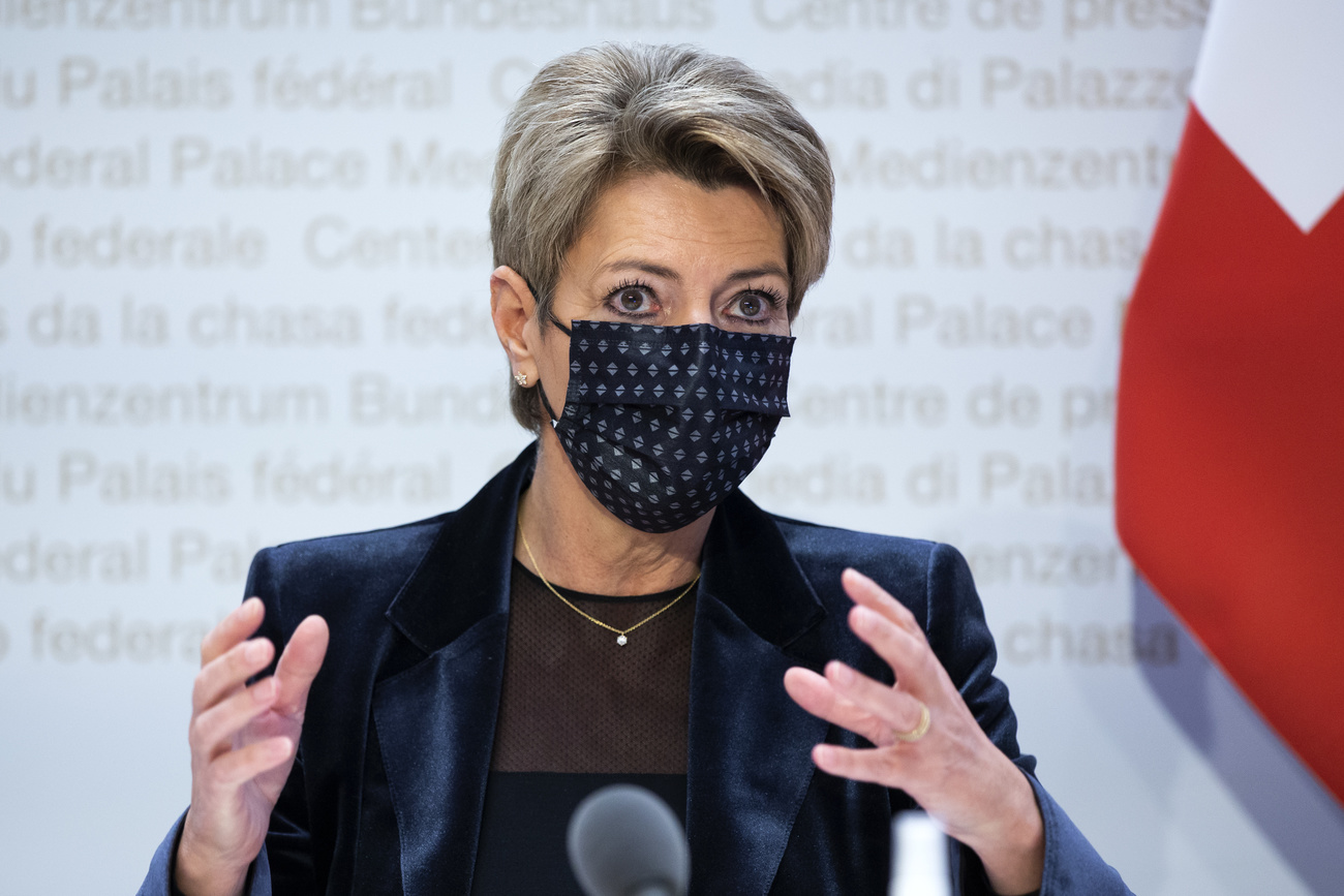 Primo piano di Karin Keller-Sutter con mascherina scura; scritta Palazzo federale sul fondo e bandiera CH accanto