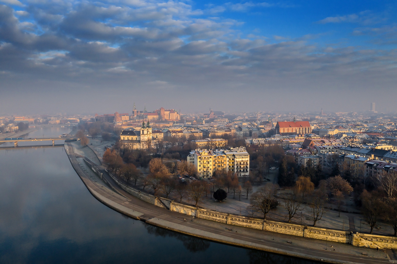 Vista panoramica di una città costeggiata da un fiume; si distinguono in cielo nubi da inquinamento