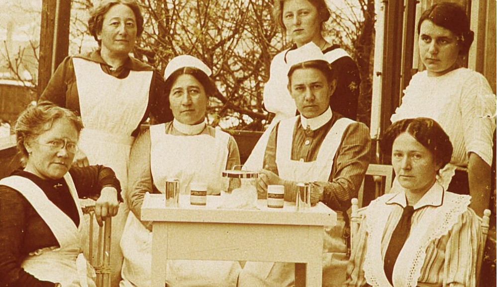 Ärztin mit drei Schwestern, sitzend. Stehend: drei Schülerinnen