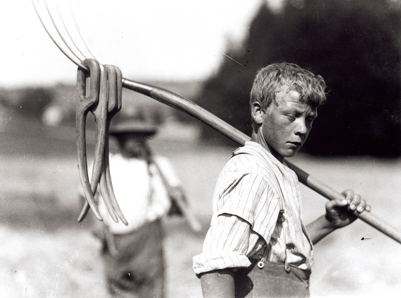 صبي يحمل مذراة على كتفة في مزرعة