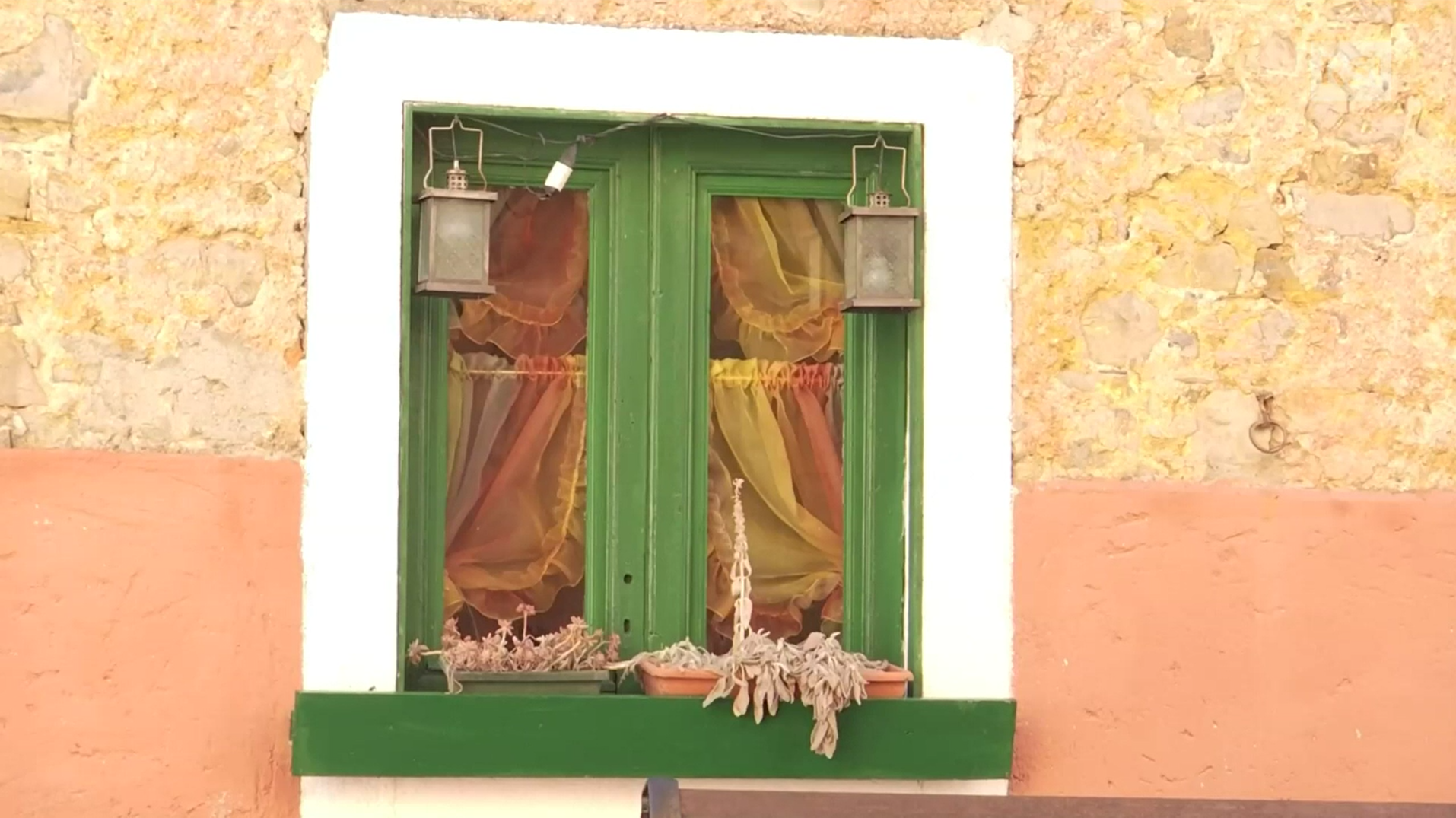 Casa con pareti gialle e rosse; primo piano di finestra con infissi e davanzale verdi, cornice bianca; tendine