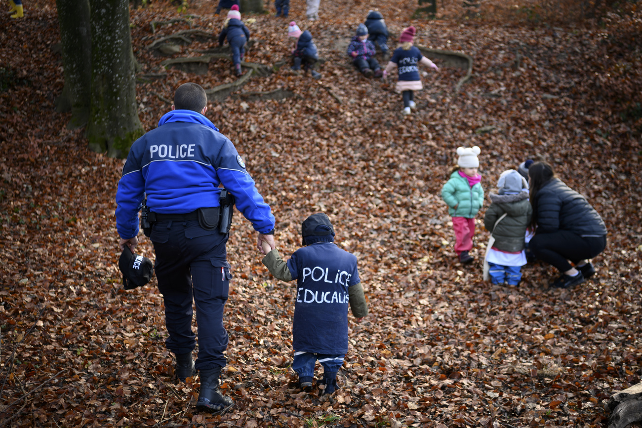 Poliziotto accompagna per mano bambino di 2-4 anni che indossa maglietta con scritta Police Educalis sul dorso