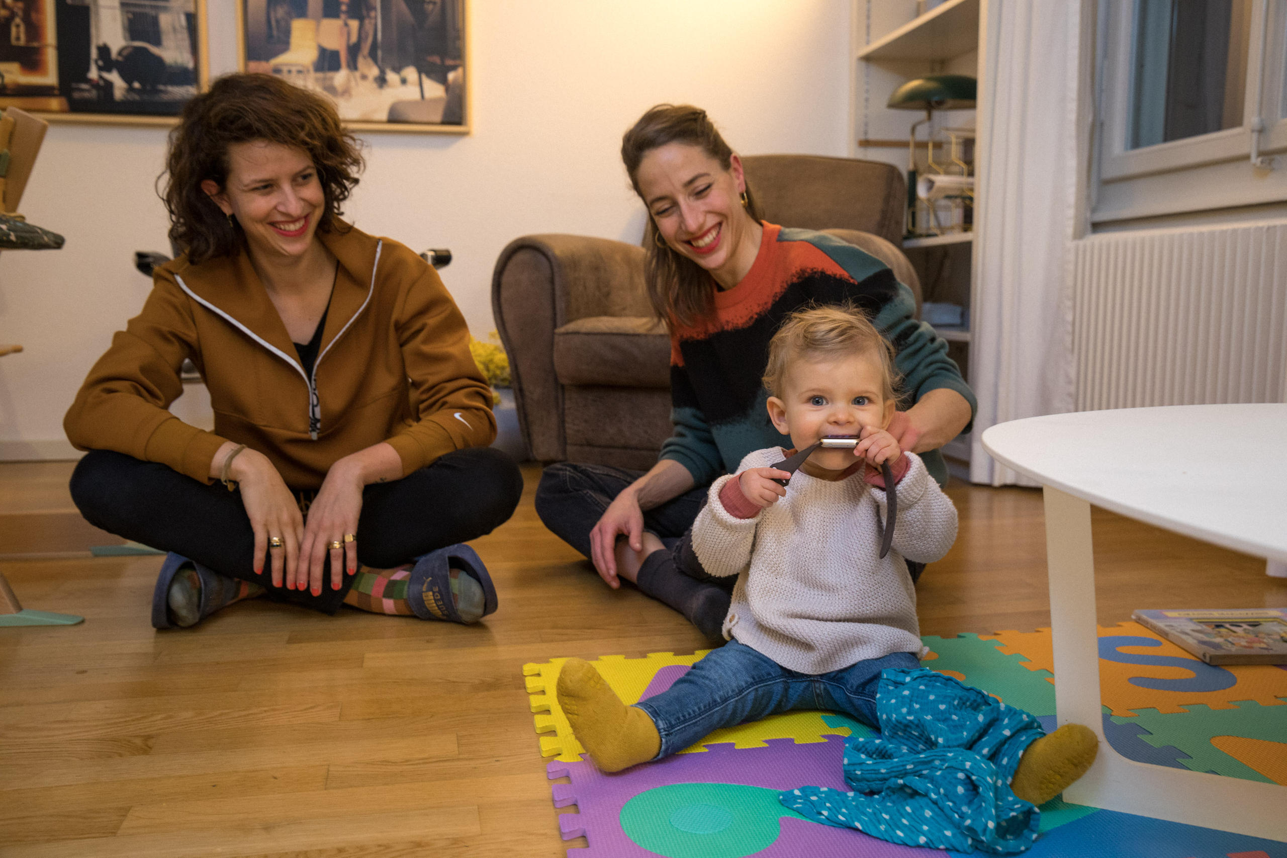 Ambra joue avec une montre assise parterre entourée de ses deux mamans