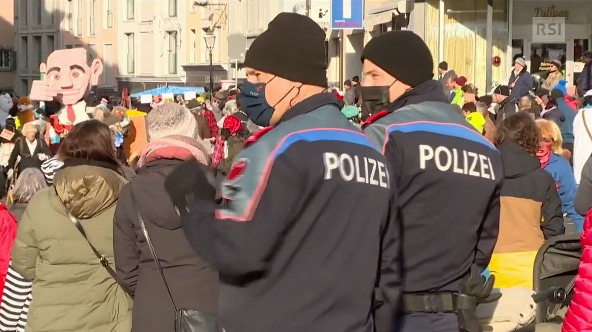 Due agenti di polizia di schiena in una piazza piena di gente in maschera