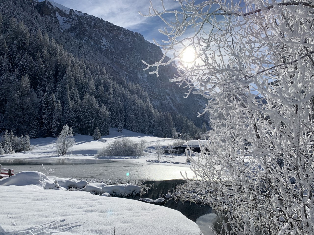 A snowy mountain scene, with frost covered branches in front of a frozen lake