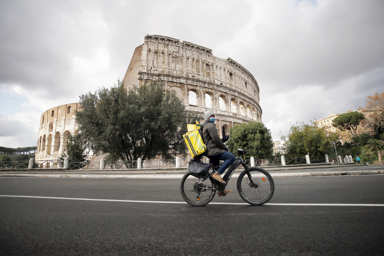 Colosseo in un giorno di tempo nuvoloso; sulla strada, transita un rider in bicicletta.