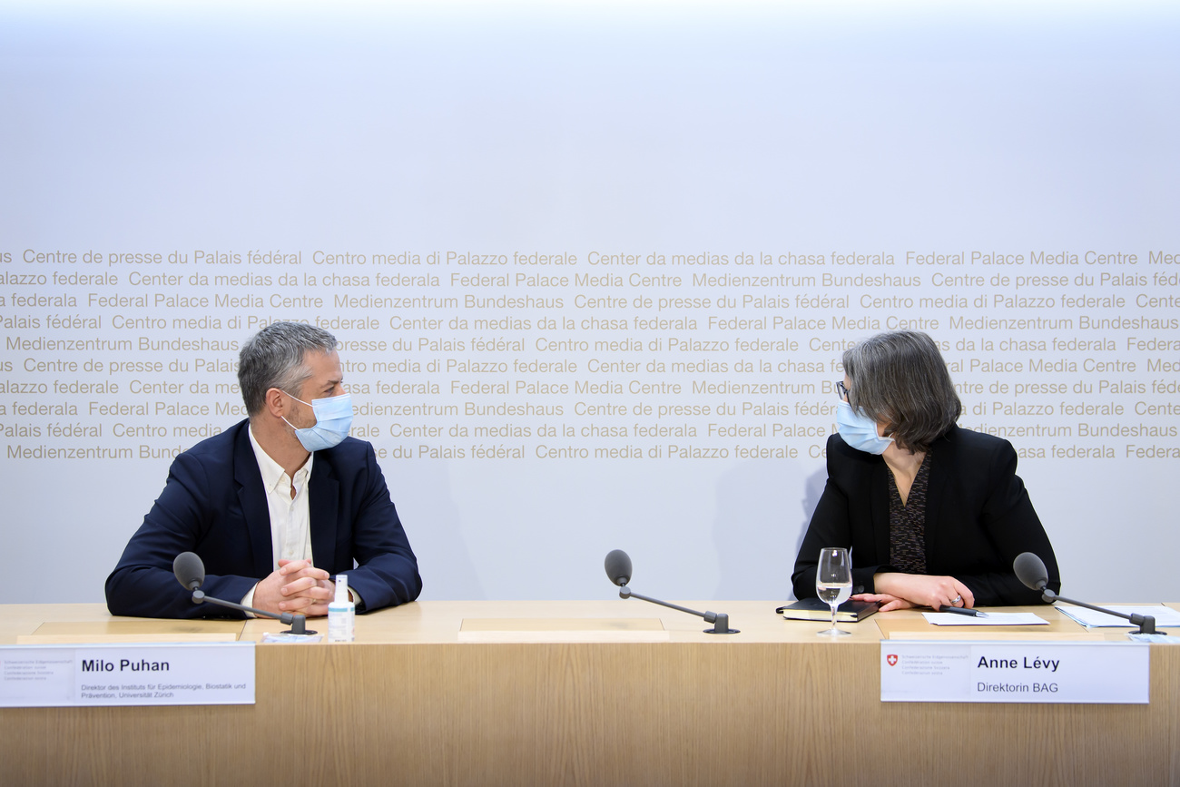 Un uomo e una donna con mascherina al banco della sala conferenze stampa di Palazzo federale si guardano