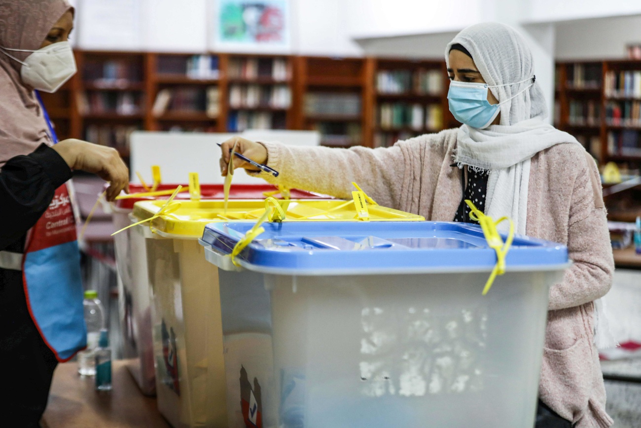 donne con mascherina e velo inseriscono la scheda elettorale nell urna