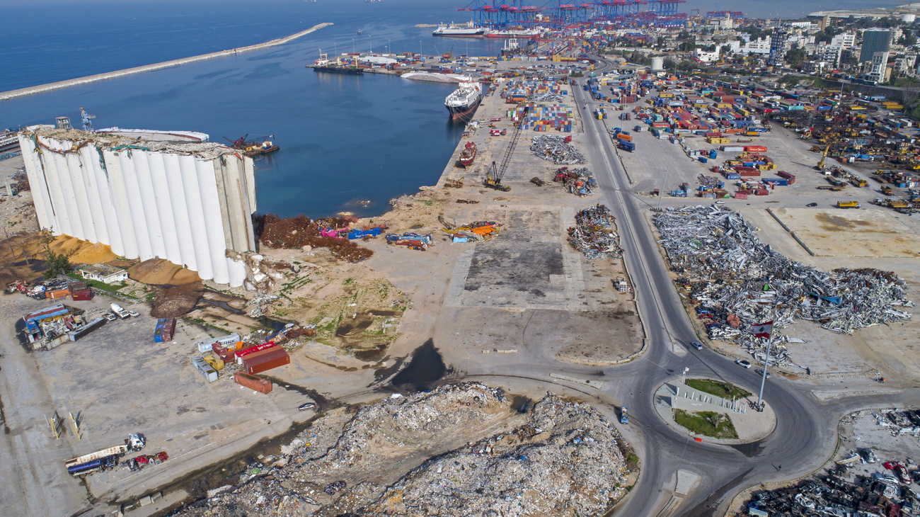 Veduta aerea di una spianata di cemento con rovine di silos e, in lontananza, container navali depositati
