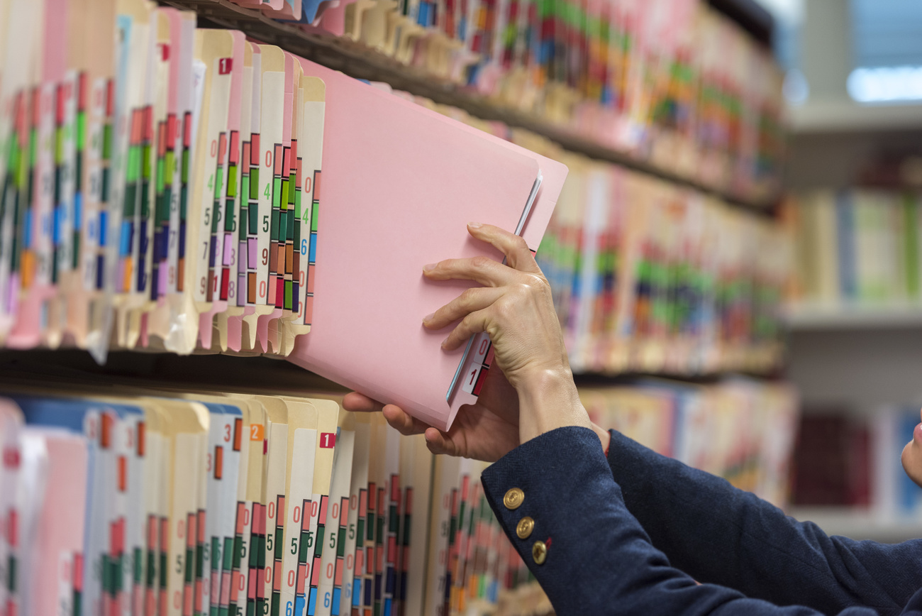 Scaffale di archivio con mappette colorate e numerate; mano di donna ne estrae una
