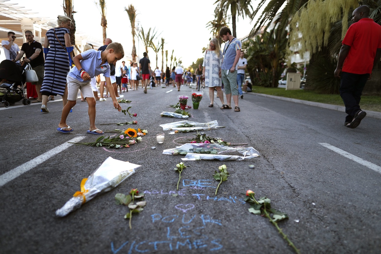 Bambini posano fiori su strada di lungomare, sulla quale giacciono già mazzi di fiori e messaggi di cordoglio