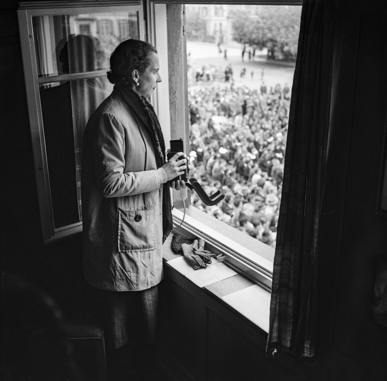 Femme à un balcon observant une foule.