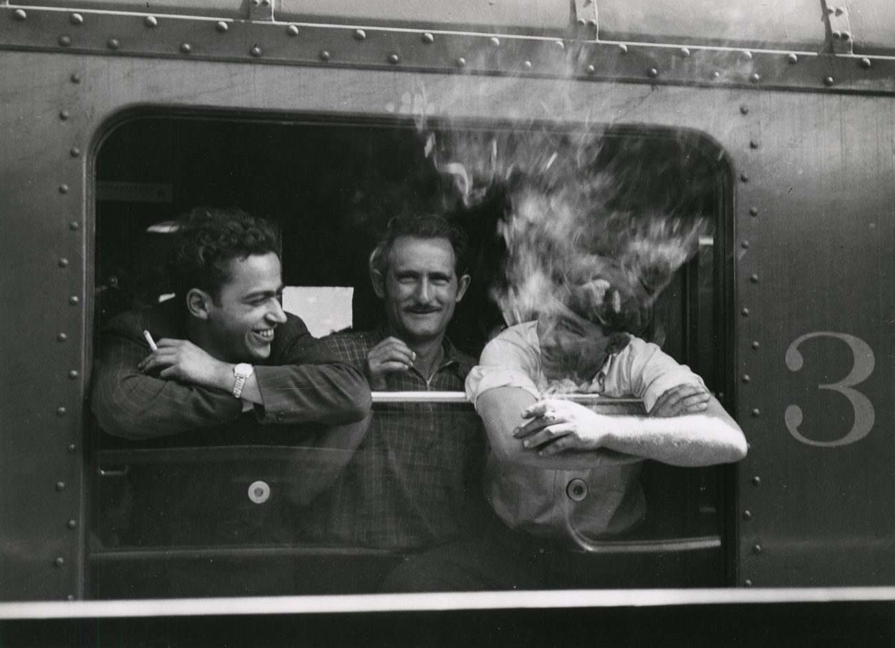 Tres hombres fuman asomados por la ventanilla de un tren