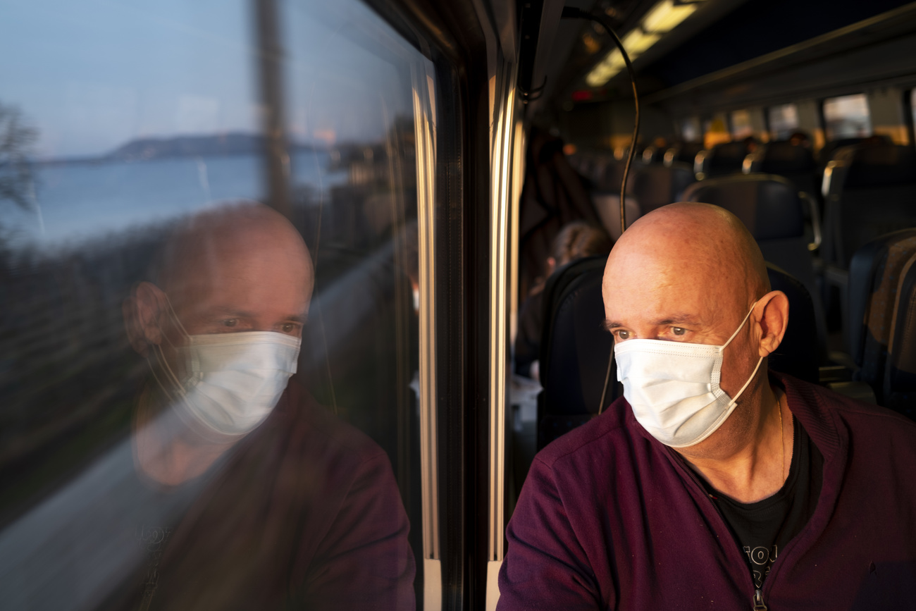 Pasajero de tren com mascarilla mira a través de la ventana. Su rostro se refleja en el vidrio.