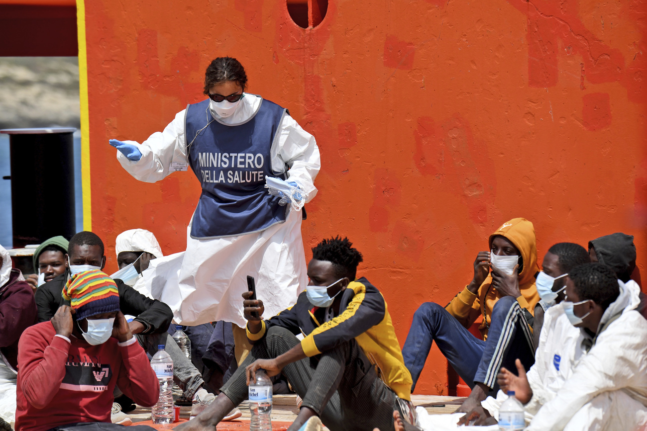 Una dipendente del ministero della salute distribuisce mascherina ai migranti.