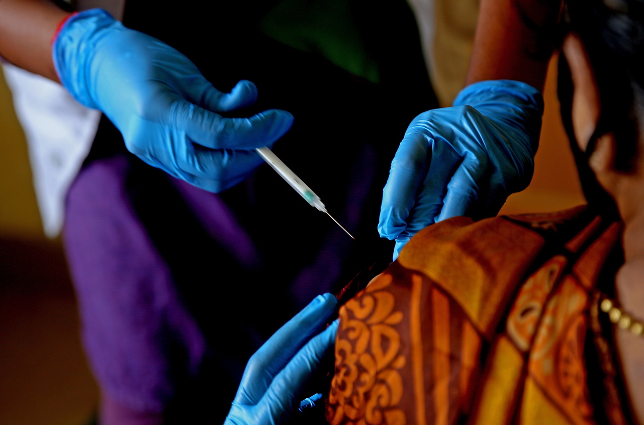 Donna riceve da operatrice sanitaria una dose di vaccino; si intuisce da abiti e gioielli che si è in Paese Asia meridionale