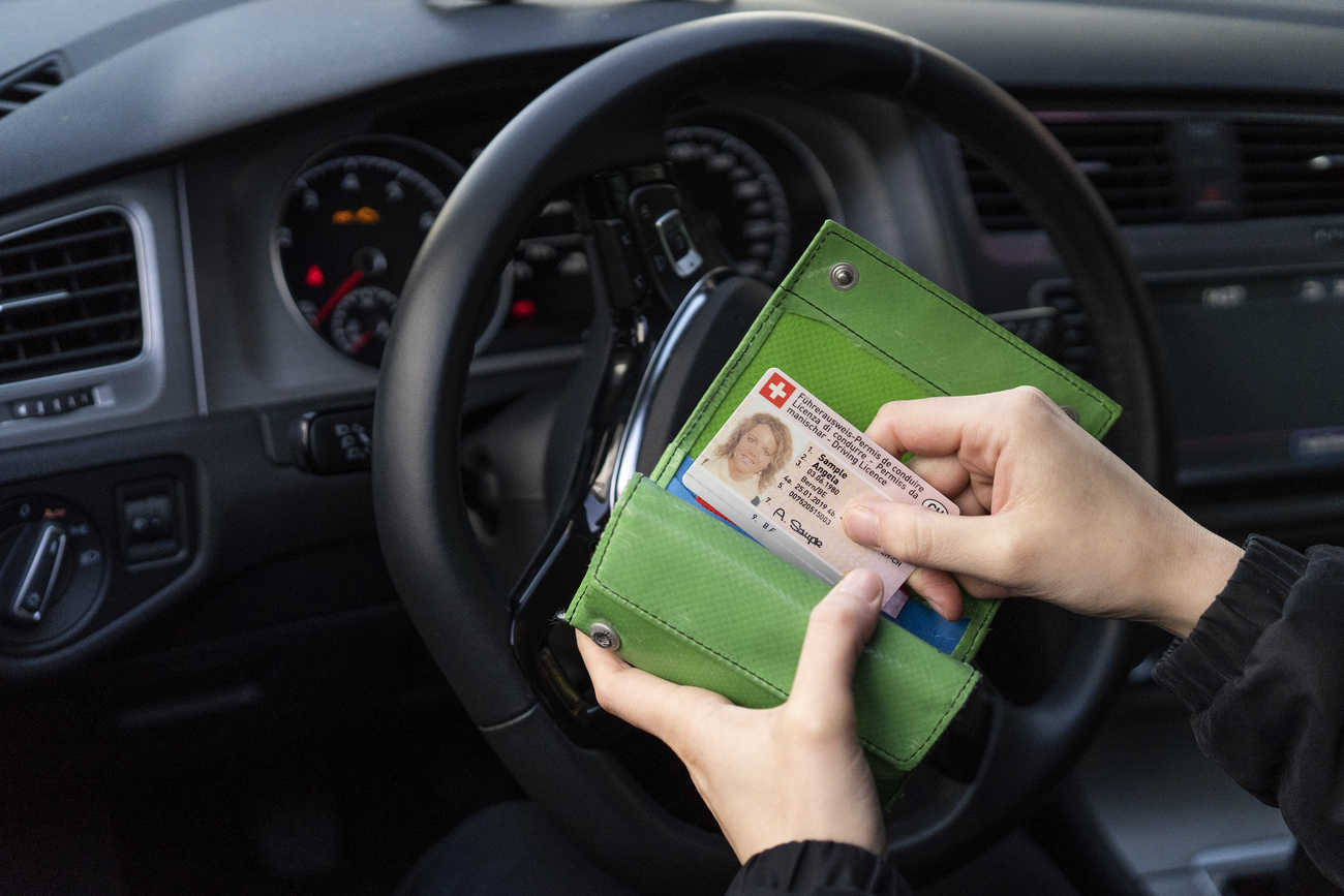 Conducente (donna) in un abitacolo d automobile estrae da un portafogli verde la patente svizzera
