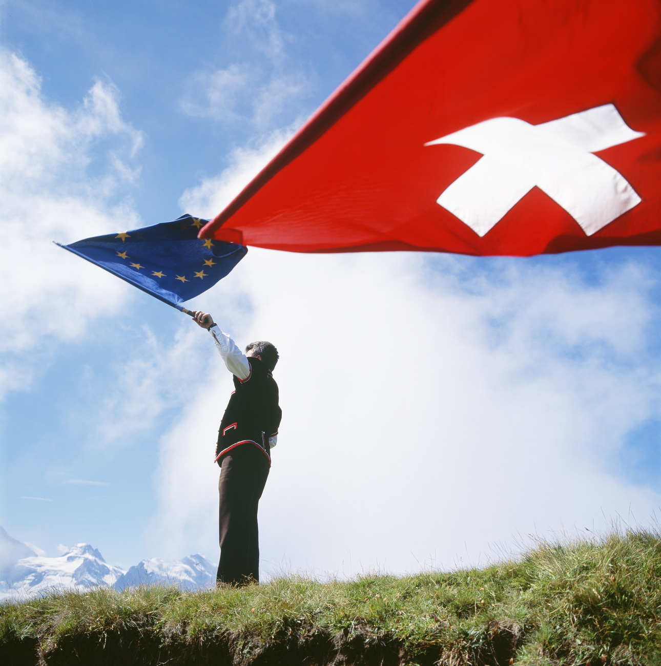 Un hombre en la cima de una montaña con las banderas europea y suiza