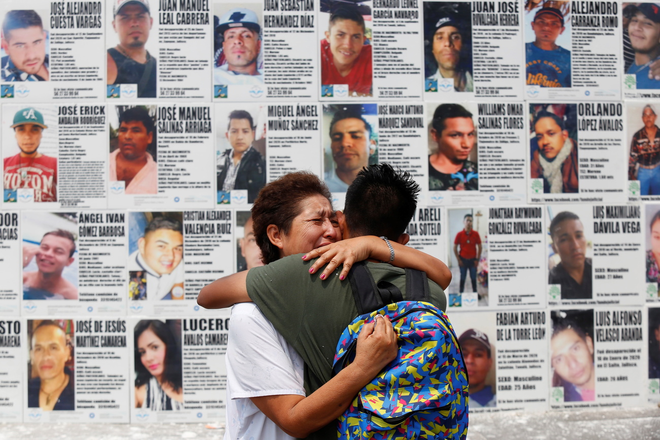 woman reunited with her son in mexico, hug in front of wall with posters of missing people