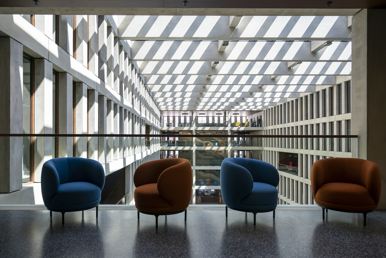 Interni di edificio brutalista con cortile interno e soffitto a griglia; in primo piano poltroncine colorate