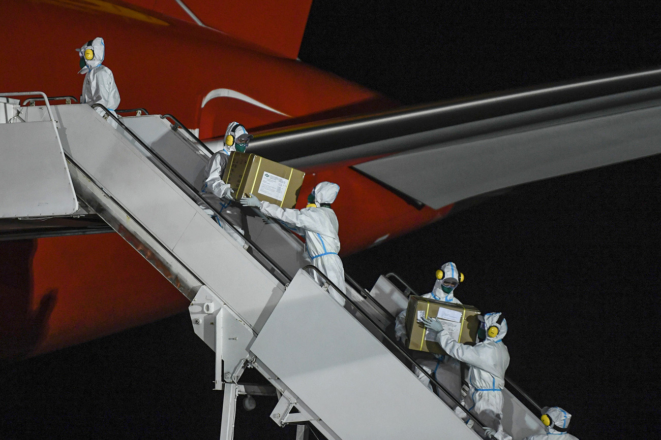 People in white protective clothing passing boxes up the ramp of an airplane.